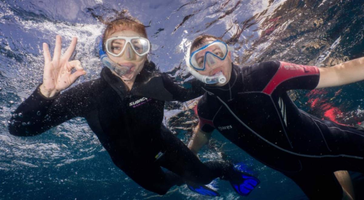 Two smiling snorkelers in wetsuits underwater in Tenerife