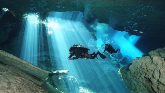 Divers descending through shafts of sunlight into a cenote cavern near Playa del Carmen